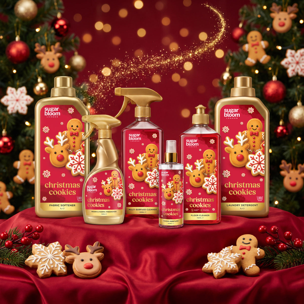 A coordinated set of Sugar Bloom 'Christmas Cookies' home fragrance products arranged on a red satin surface with holiday decorations, including a large laundry detergent bottle, spray bottle, room spray, and smaller bottles, all featuring gingerbread-themed labels.